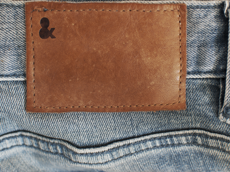 Brown blank leather label tag on denim pants background. Blank